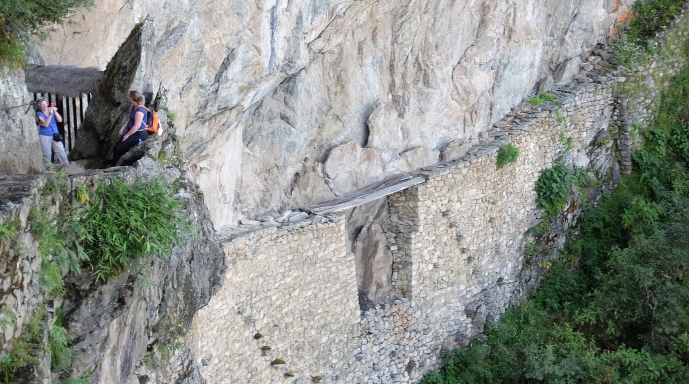 Sendero en cornisa y puente de troncos del Puente Inka en la pared vertical de Machu Picchu